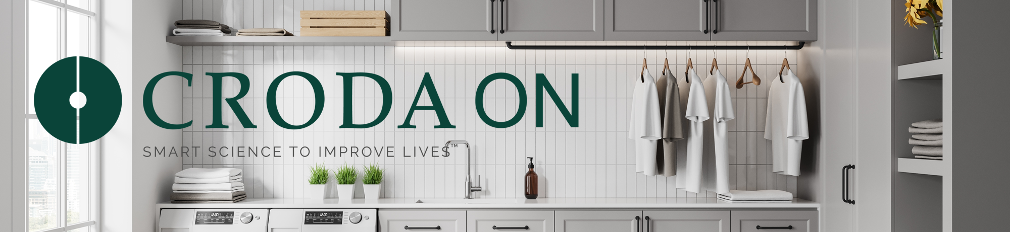 A very clean laundry room with washing machine and tumble dryer, laundry basket, clean clothes hanging up and a sink. The words "Croda On - Smat science to improve lives" are written across it.